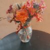 A clear glass vase filled with a vibrant bouquet featuring an orange rose, red and blush blooms, and cream accents—styled for poetic flower delivery in Cincinnati Ohio and Northern Kentucky.