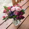 Pink roses, red alstroemeria, purple asters, and magenta pom-pom mums in a glass vase