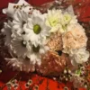 Bouquet of white daisies, peach carnations, and greenery wrapped in polka-dotted paper against a red background