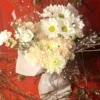 White daisies and peach carnations wrapped in polka‑dot paper against a red background.