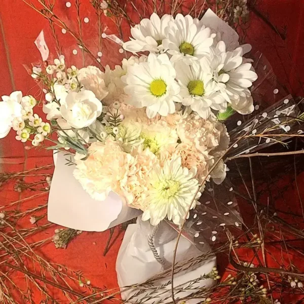 White daisies and peach carnations wrapped in polka‑dot paper against a red background.