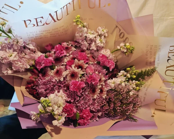 Lavender-themed bouquet featuring lavender poms, magenta mini carnations, purple waxflower, and a fresh lavender stem wrapped in elegant paper