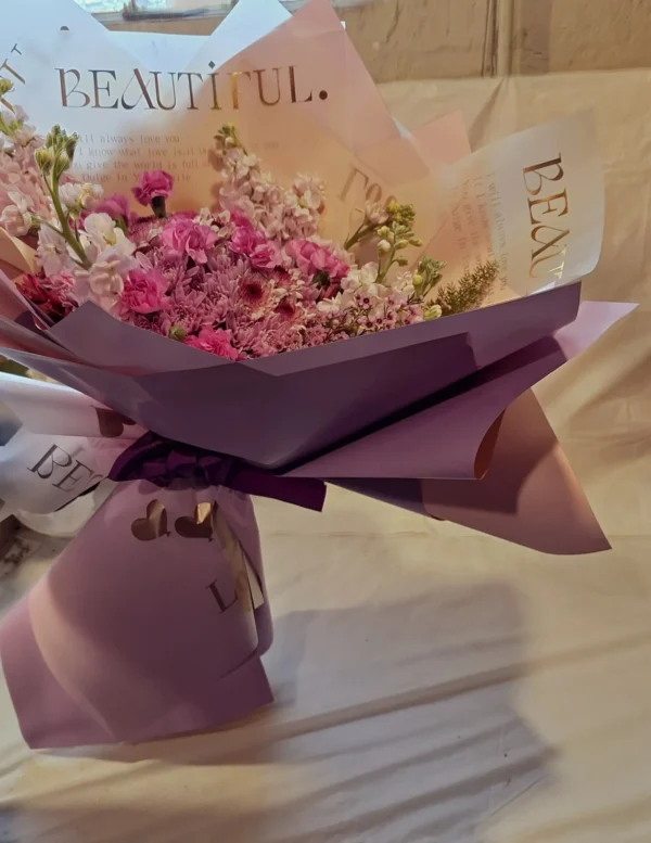 Lavender-themed bouquet featuring lavender poms, magenta mini carnations, purple waxflower, and a fresh lavender stem wrapped in elegant paper