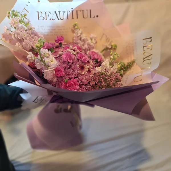 Lavender-themed bouquet featuring lavender poms, magenta mini carnations, purple waxflower, and a fresh lavender stem wrapped in elegant paper