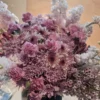 Lavender-themed bouquet featuring lavender poms, magenta mini carnations, purple waxflower, and a fresh lavender stem wrapped in elegant paper