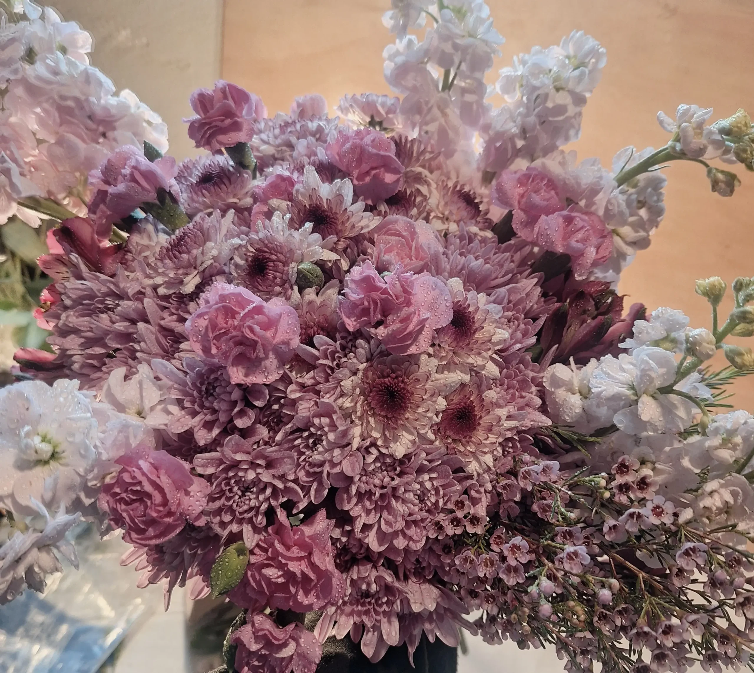 Lavender-themed bouquet featuring lavender poms, magenta mini carnations, purple waxflower, and a fresh lavender stem wrapped in elegant paper