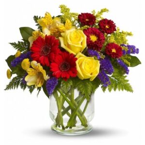 Clear glass vase with yellow roses, red gerbera daisies, purple statice, yellow alstroemeria, and green foliage arranged fresh for local Cincinnati florist delivery