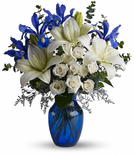 Blue glass vase with white lilies, white roses, and blue irises arranged fresh with green foliage for Cincinnati flower delivery.