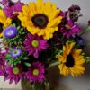 Handcrafted bouquet of sunflowers, purple daisies, and blue asters in a clear vase, delivered fresh by a local Cincinnati florist.