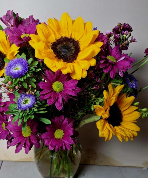 Handcrafted bouquet of sunflowers, purple daisies, and blue asters in a clear vase, delivered fresh by a local Cincinnati florist.