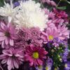 White chrysanthemums, pink daisies, magenta daisies, and purple asters arranged with lush green foliage in a vibrant Cincinnati bouquet.
