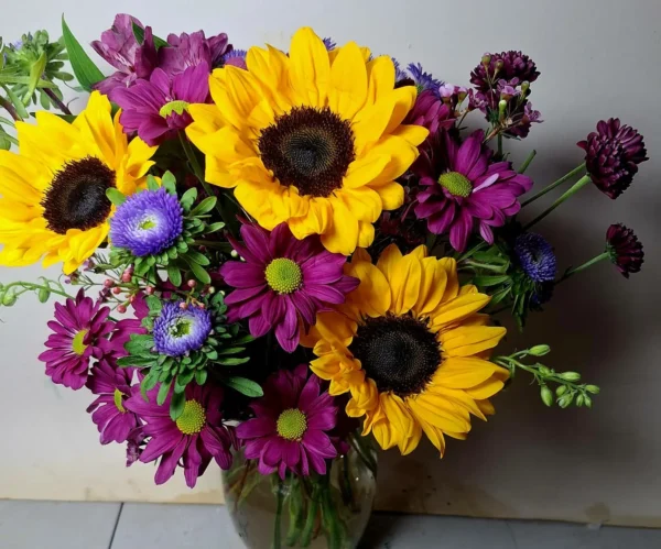 Handcrafted bouquet of sunflowers, purple daisies, and blue asters in a clear vase, delivered fresh by a local Cincinnati florist.