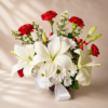 Elegant floral arrangement with white lilies, daisies, and red carnations in a red vase with satin ribbon