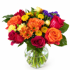 Rainbow Vase bouquet with orange roses, red roses, yellow daisies, purple accents, and lush greenery in a clear glass vase.