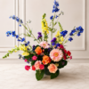 Cincinnati Colorburst bouquet with orange roses, pink gerbera daisies, peach carnations, bright pink mini carnations, yellow snapdragons, blue delphiniums, and purple accents, delivered fresh across Cincinnati and Northern Kentucky by allthepeoplesflowers.com