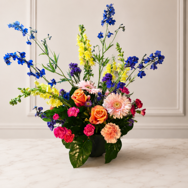 Cincinnati Colorburst bouquet with orange roses, pink gerbera daisies, peach carnations, bright pink mini carnations, yellow snapdragons, blue delphiniums, and purple accents, delivered fresh across Cincinnati and Northern Kentucky by allthepeoplesflowers.com