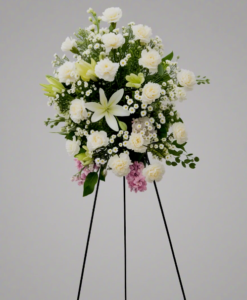 Graceful Farewell standing spray with white lilies, carnations, and soft pink accents, handcrafted for sympathy and remembrance by Local Cincinnati Florist.