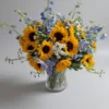 Morning Walk bouquet with sunflowers, blue delphinium, and white daisies in a clear glass vase.