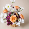 Patience and Love floral basket with peach roses, white daisies, and purple chrysanthemums arranged in a wicker basket with ribbons.