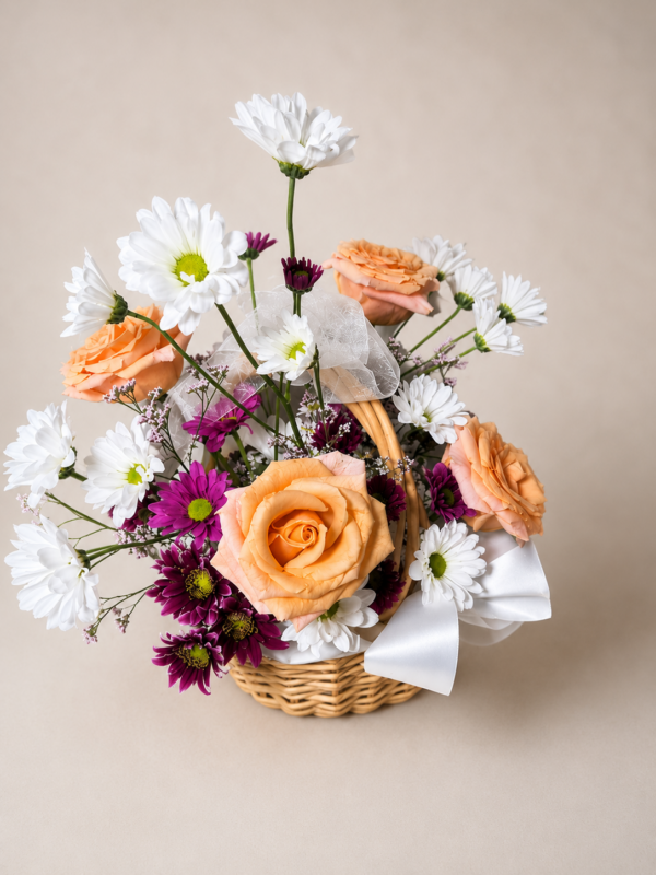 Patience and Love floral basket with peach roses, white daisies, and purple chrysanthemums arranged in a wicker basket with ribbons.