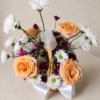 Patience and Love floral basket with peach roses, white daisies, and purple chrysanthemums arranged in a wicker basket with ribbons.