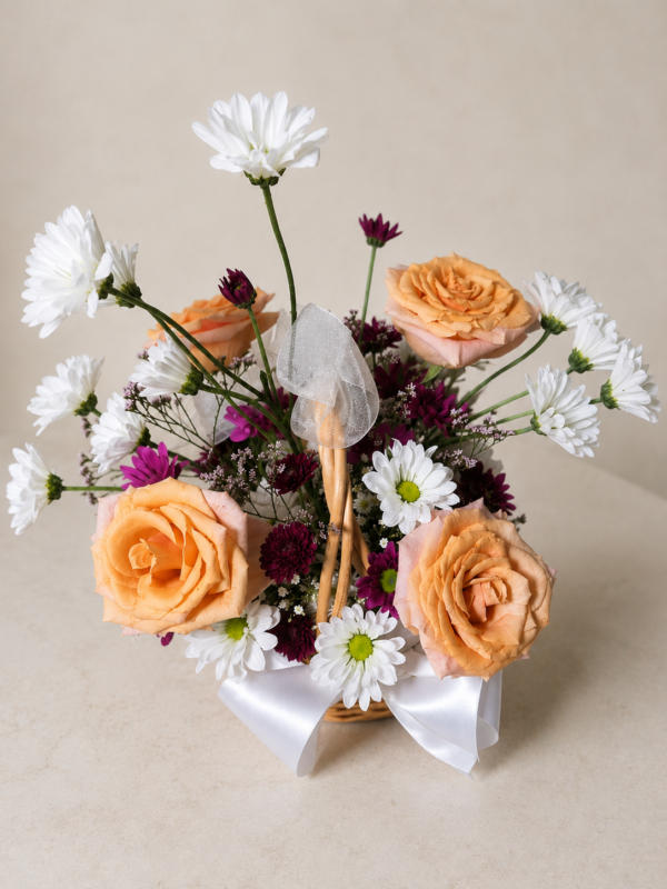 Patience and Love floral basket with peach roses, white daisies, and purple chrysanthemums arranged in a wicker basket with ribbons.