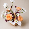 Patience and Love floral basket with peach roses, white daisies, and purple chrysanthemums arranged in a wicker basket with ribbons.