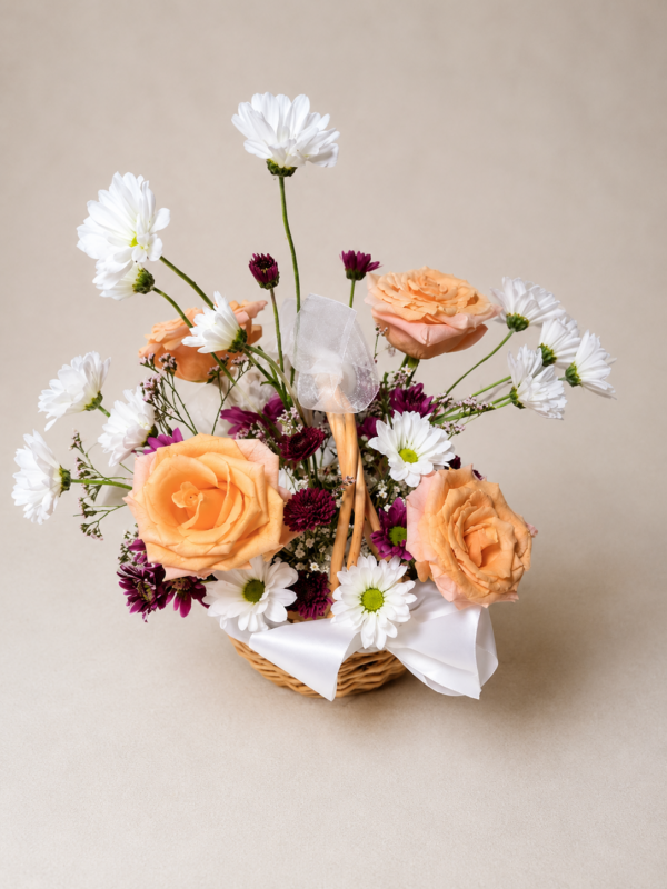 Patience and Love floral basket with peach roses, white daisies, and purple chrysanthemums arranged in a wicker basket with ribbons.