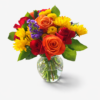 Rainbow Vase bouquet with orange roses, red roses, yellow daisies, purple accents, and lush greenery in a clear glass vase.