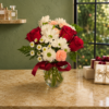 Cool Pretty Girl Bouquet of red roses, white daisies, and pink carnations in a glass vase with greenery, tied with a red ribbon, displayed indoors with natural light.