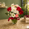 Cool Pretty Girl Bouquet of red roses, white daisies, and pink carnations in a glass vase with greenery, tied with a red ribbon, displayed indoors with natural light.