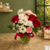 Cool Pretty Girl Bouquet of red roses, white daisies, and pink carnations in a glass vase with greenery, tied with a red ribbon, displayed indoors with natural light.