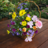 Basket of fresh seasonal flowers arranged one‑sided on a brown wooden table in a garden setting, symbolizing Floral Paradise.