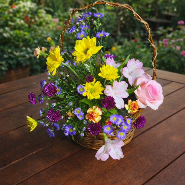 Basket of fresh seasonal flowers arranged one‑sided on a brown wooden table in a garden setting, symbolizing Floral Paradise.