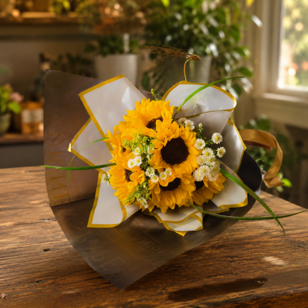 Fresh bouquet of sunflowers, white daisies, and greenery wrapped in gray and gold paper, displayed on a rustic wooden surface with warm indoor light.