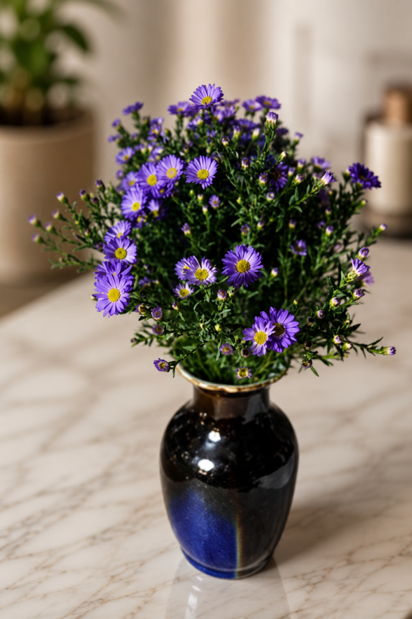Something about Mary Fresh purple daisy bouquet with bright yellow centers arranged in a deep blue ceramic vase, styled on polished marble surface with soft natural background, elegant floral arrangement for secure Cincinnati delivery