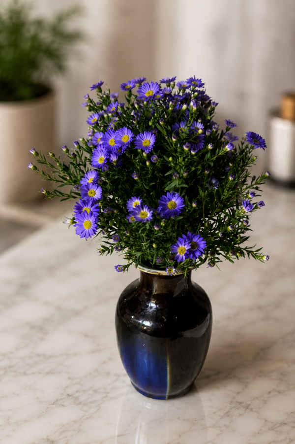 Something about Mary Fresh purple daisy bouquet with bright yellow centers arranged in a deep blue ceramic vase, styled on polished marble surface with soft natural background, elegant floral arrangement for secure Cincinnati delivery
