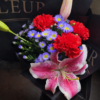 The Raven bouquet with red carnations, purple asters, and pink stargazer lily wrapped in dark paper