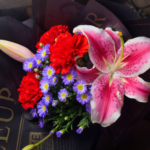 The Raven bouquet with red carnations, purple asters, and pink stargazer lily wrapped in dark paper