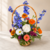 Wildflower Season Zinnia Basket with bright zinnias, delphiniums, roses, daisies, and greenery arranged in a woven basket on marble surface.