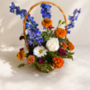 Wildflower Season Zinnia Basket with bright zinnias, delphiniums, roses, daisies, and greenery arranged in a woven basket on marble surface.