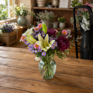 Autumn Sunset Designers Choice bouquet with chrysanthemums, lilies, carnations, and daisies in warm sunset tones, handcrafted in a clear glass vase.
