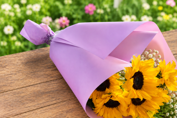 Cascading Sun bouquet featuring radiant sunflowers, lavender accents, and smaller yellow blooms, wrapped in pastel paper, handcrafted by allthepeoplesflowers.com for Cincinnati and Northern Kentucky delivery.
