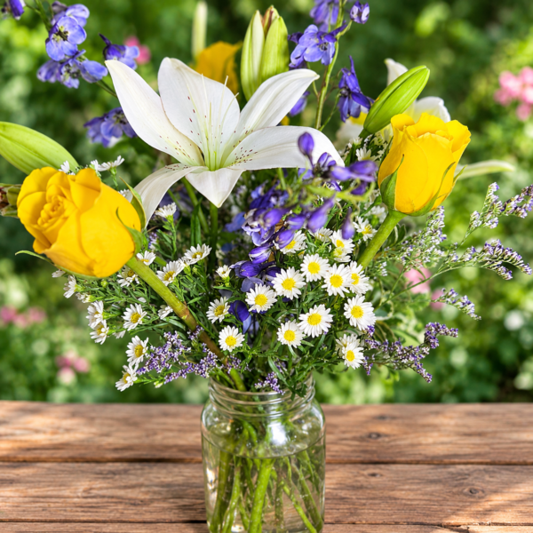 Endless Skies bouquet with yellow roses, white lilies, daisies, and purple blooms in a clear glass jar