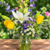 Endless Skies bouquet with yellow roses, white lilies, daisies, and purple blooms in a clear glass jar