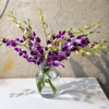 Elegant Orchid bouquet with purple and white orchids in a clear vase on a wooden table, surrounded by lush garden foliage.
