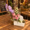 Coffee and Flowers To Go Supreme arrangement with pink roses, stock flowers, daisies, and lavender sprigs in a white container on a café table.