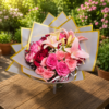 Elegant bouquet of pink roses, red roses, and lilies wrapped in white paper with gold trim, arranged in a glass vase.