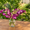 Elegant Orchid bouquet with purple and white orchids in a clear vase on a wooden table, surrounded by lush garden foliage.