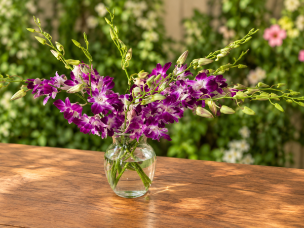 Elegant Orchid bouquet with purple and white orchids in a clear vase on a wooden table, surrounded by lush garden foliage.